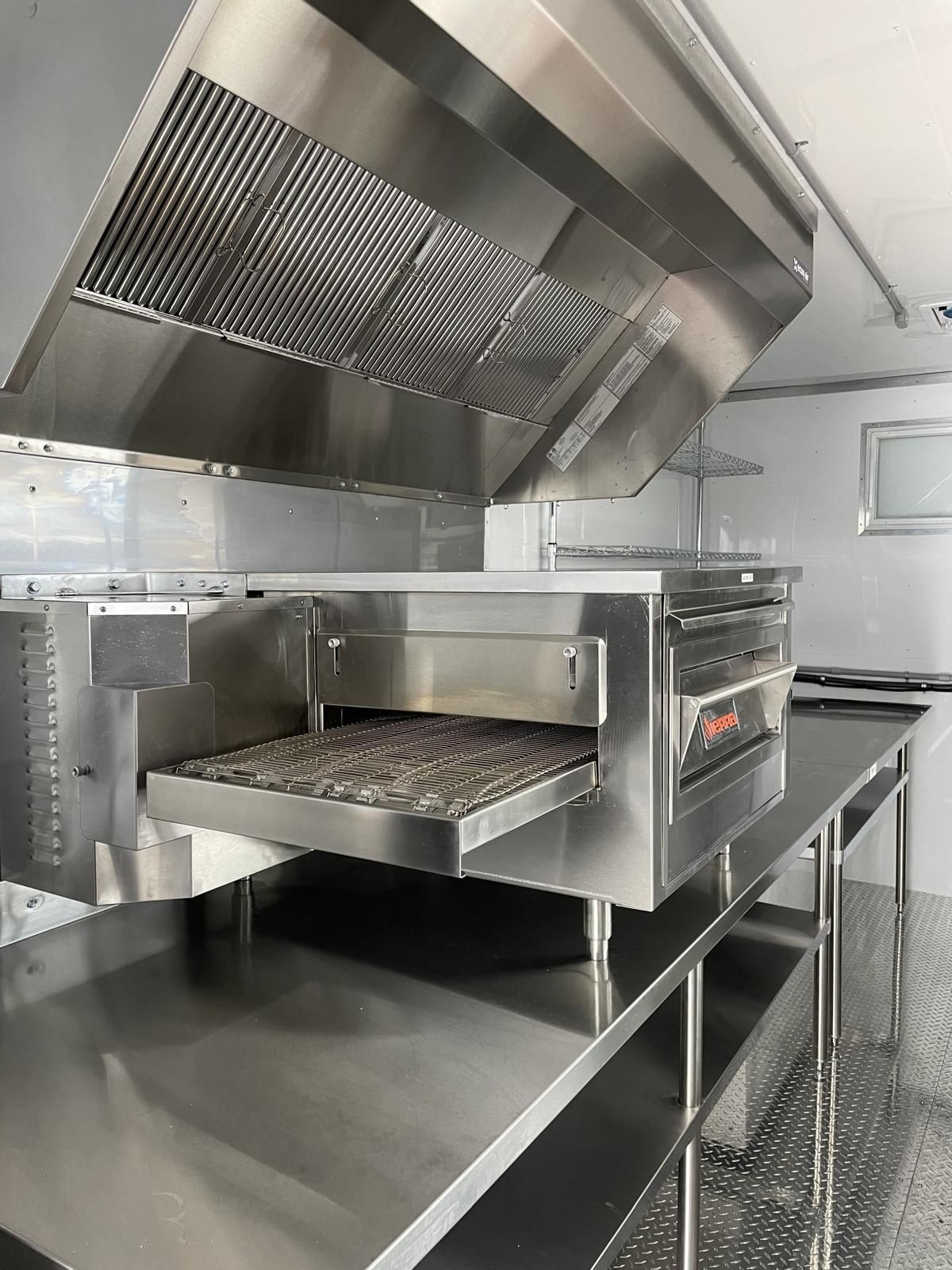 Commercial stainless steel kitchen with large ventilation hood and cooking equipment.