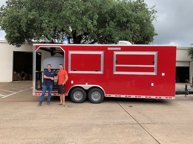 Two people standing in front of a large red trailer with open compartments.