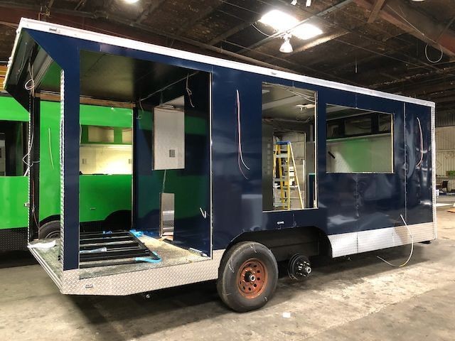 Unfinished food truck with dark blue exterior and large window openings, inside an industrial workshop.