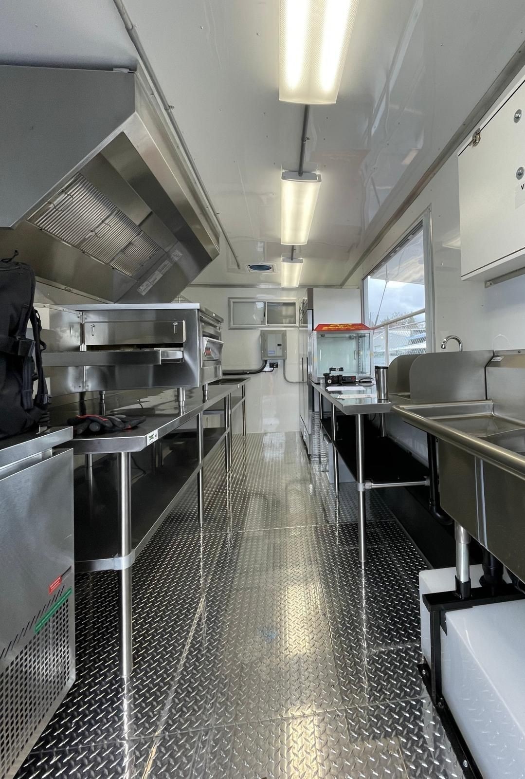 Interior of a modern food truck kitchen with stainless steel appliances and diamond plate flooring.